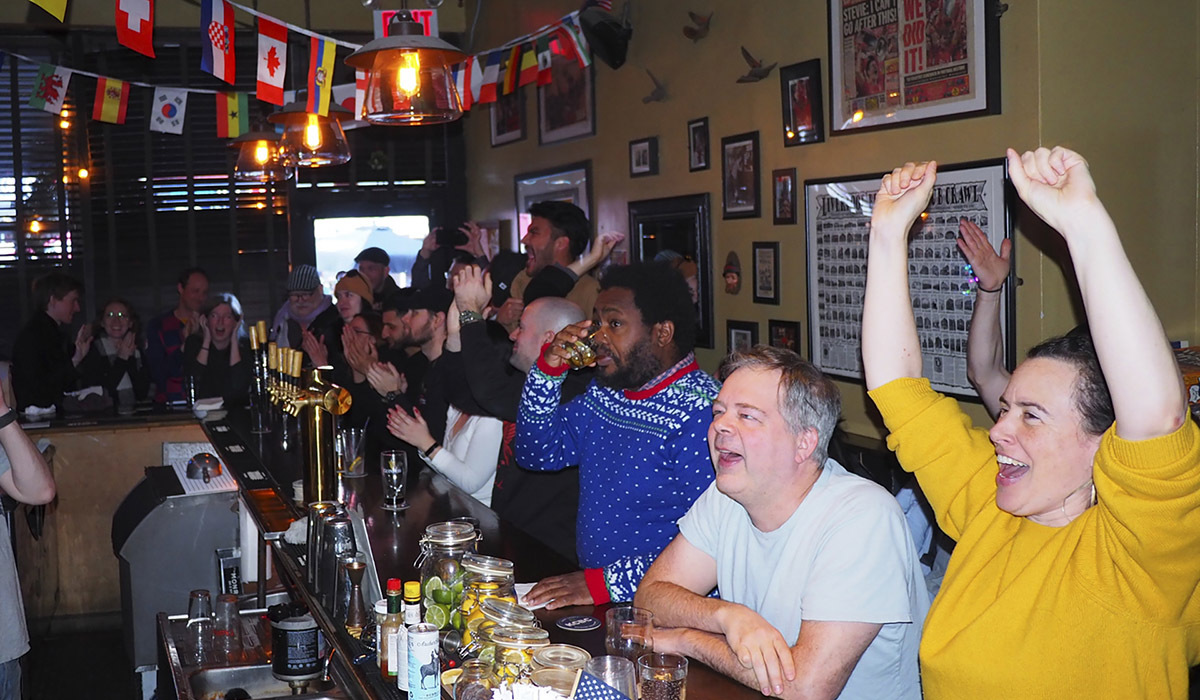 This is a photo of The Monro Pub in Brooklyn. Soccer fans are seen sitting at the bar watching a match.